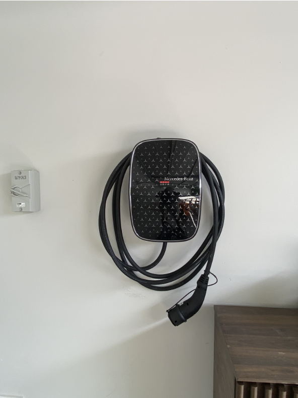Wall-mounted Mercedes-Benz EV home charger with charging cable coiled on an off-white wall