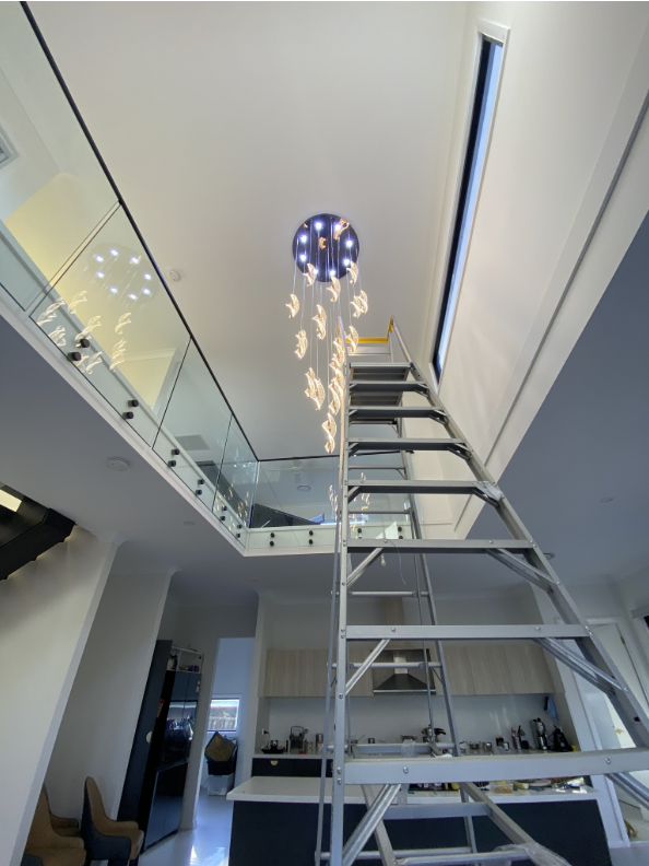 Cascading crystal spiral LED chandelier in a two-storey foyer with an extension ladder below during installation