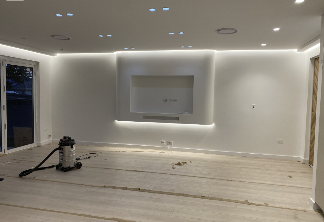Curved media wall niche with hidden warm LED backlighting around the ceiling perimeter and recessed ceiling downlights