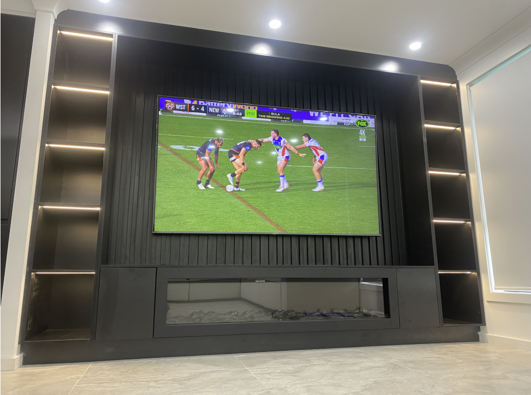 Matte black media wall with slatted backdrop, built-in linear fireplace and warm LED strip lighting under symmetrical open shelves