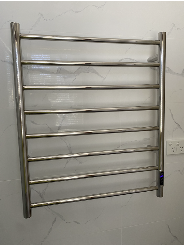 Chrome ladder-style heated towel rail with digital touch controls on a white marble-look tiled wall beside a power point
