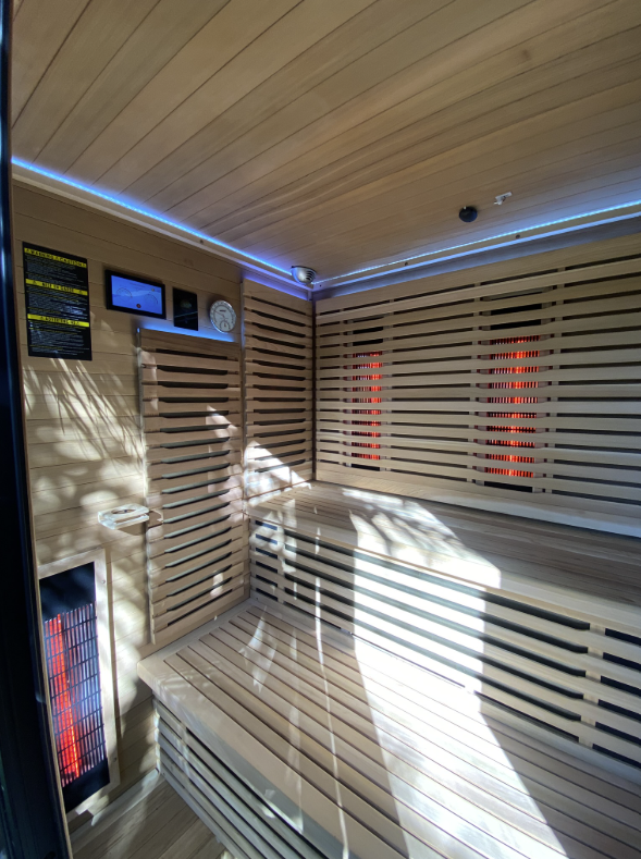 Infrared sauna interior with glowing red vertical heating panels, blue LED cove ceiling lighting and a digital control screen