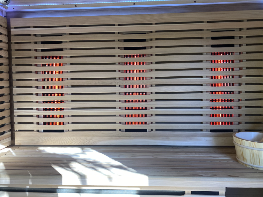 Three glowing red infrared heating panels behind horizontal wooden slats with an overhead LED light strip