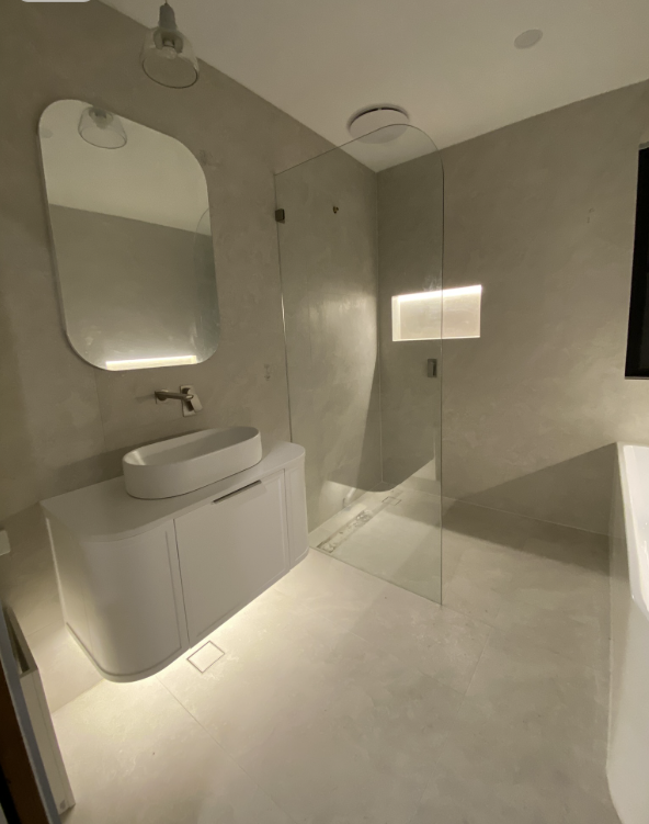 Floating vanity with warm LED underglow, capsule mirror and recessed LED shower niche beside a glass screen