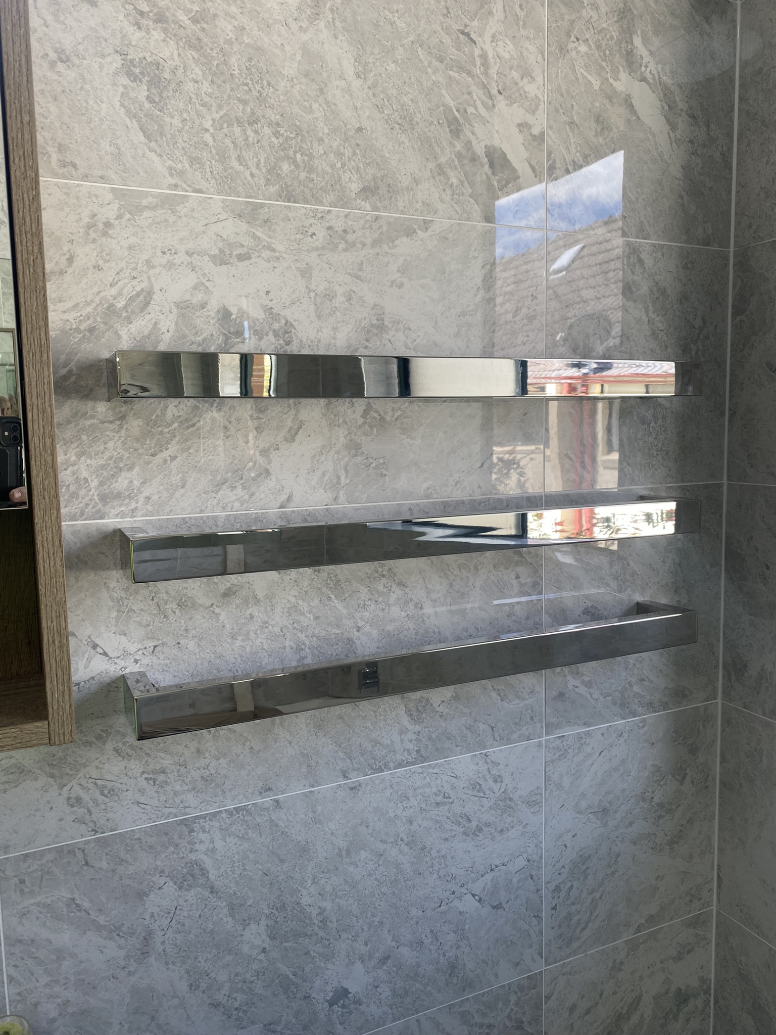 Three chrome hardwired heated towel rails mounted on a grey marble-look tiled bathroom wall
